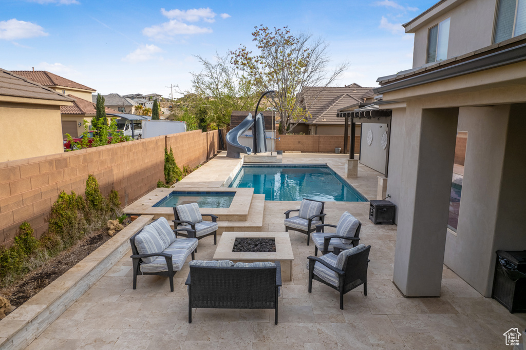 View of swimming pool featuring a water slide, a fenced backyard, an outdoor living space with a fire pit, and a patio