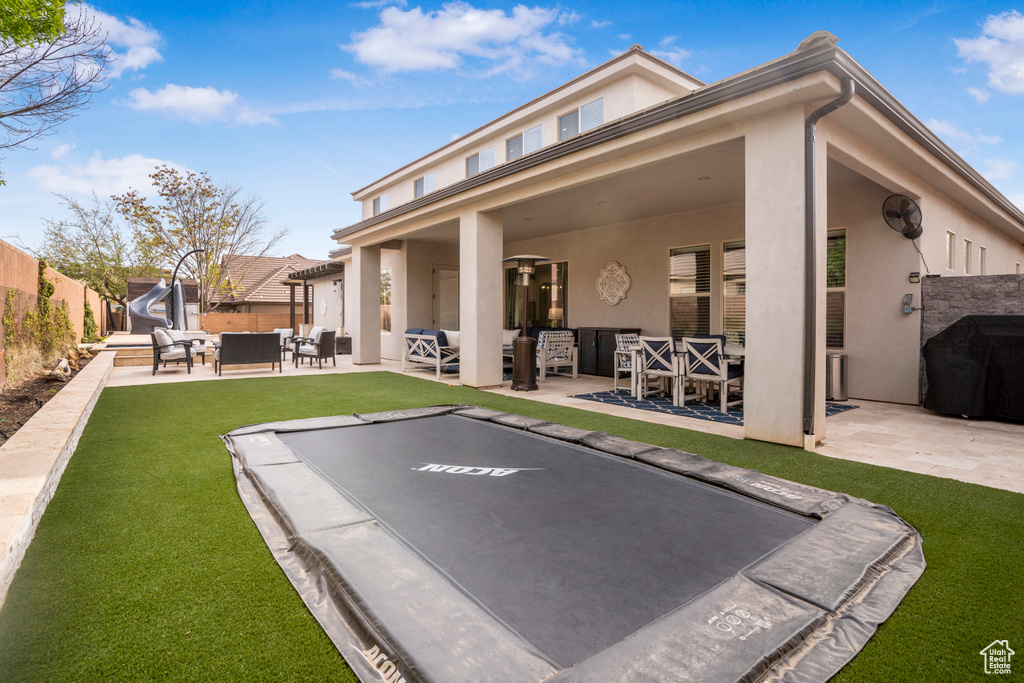Rear view of house with an outdoor living space, stucco siding, a patio area, and a trampoline