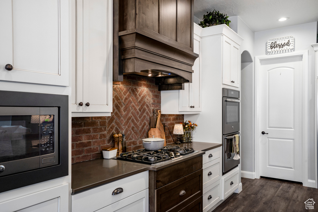 Kitchen featuring built in microwave, dark countertops, gas stovetop, dark wood-style flooring, and tasteful backsplash