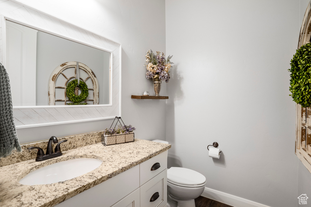 Bathroom featuring toilet, vanity, wood finished floors, and baseboards