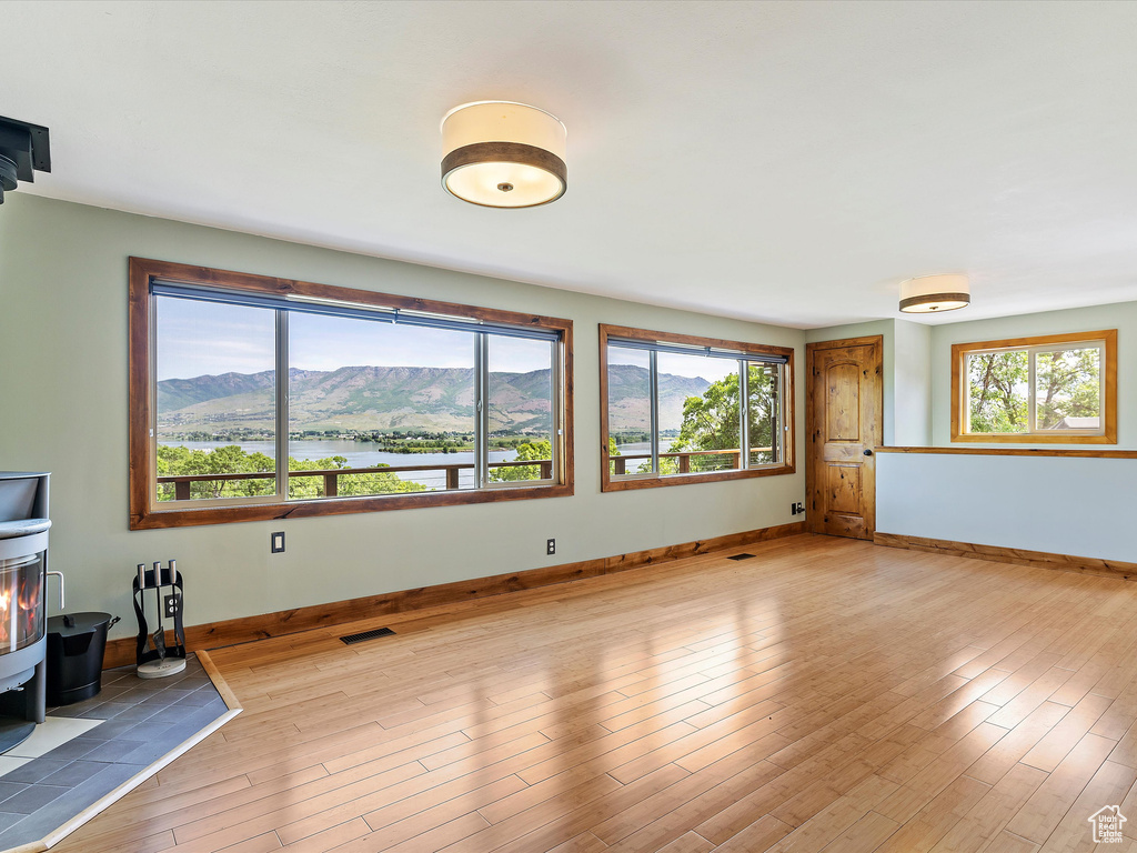 Unfurnished living room with a wood stove, wood finished floors, baseboards, and a water and mountain view