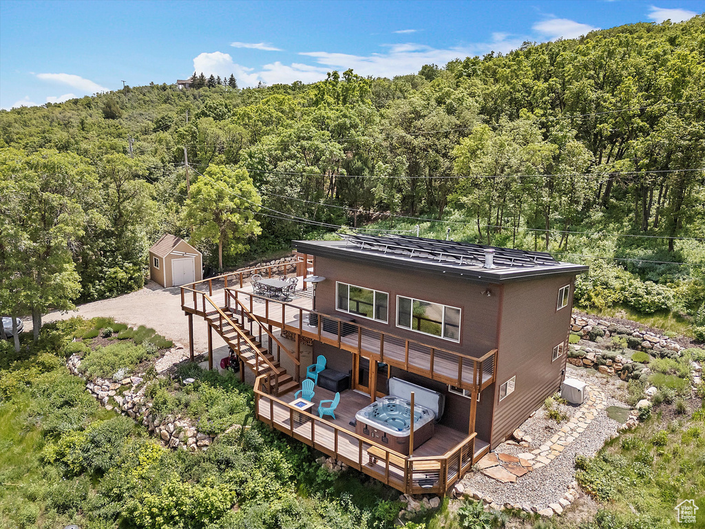 Back of property with a wooden deck, a wooded view, and a hot tub