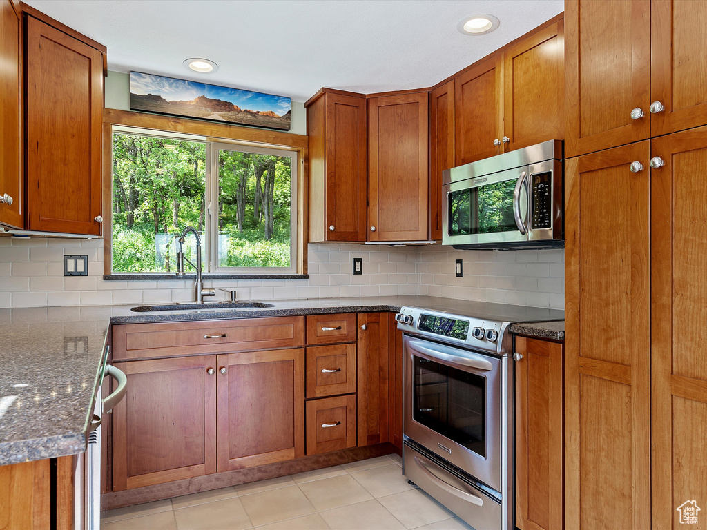 Kitchen with stainless steel appliances, a sink, brown cabinetry, and tasteful backsplash