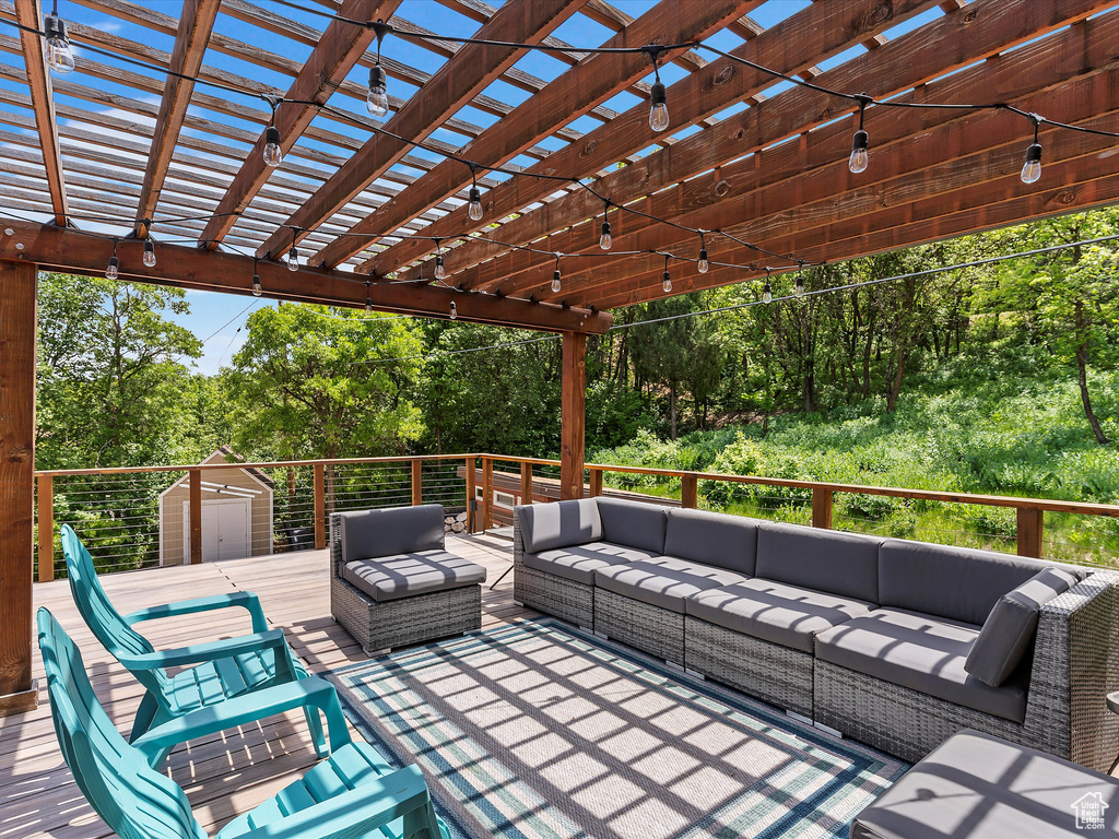 Wooden terrace featuring an outdoor hangout area, a pergola, and a storage unit