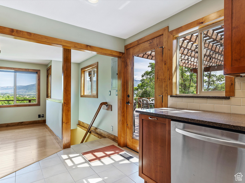 Kitchen with dishwasher, baseboards, decorative backsplash, brown cabinetry, and dark stone countertops