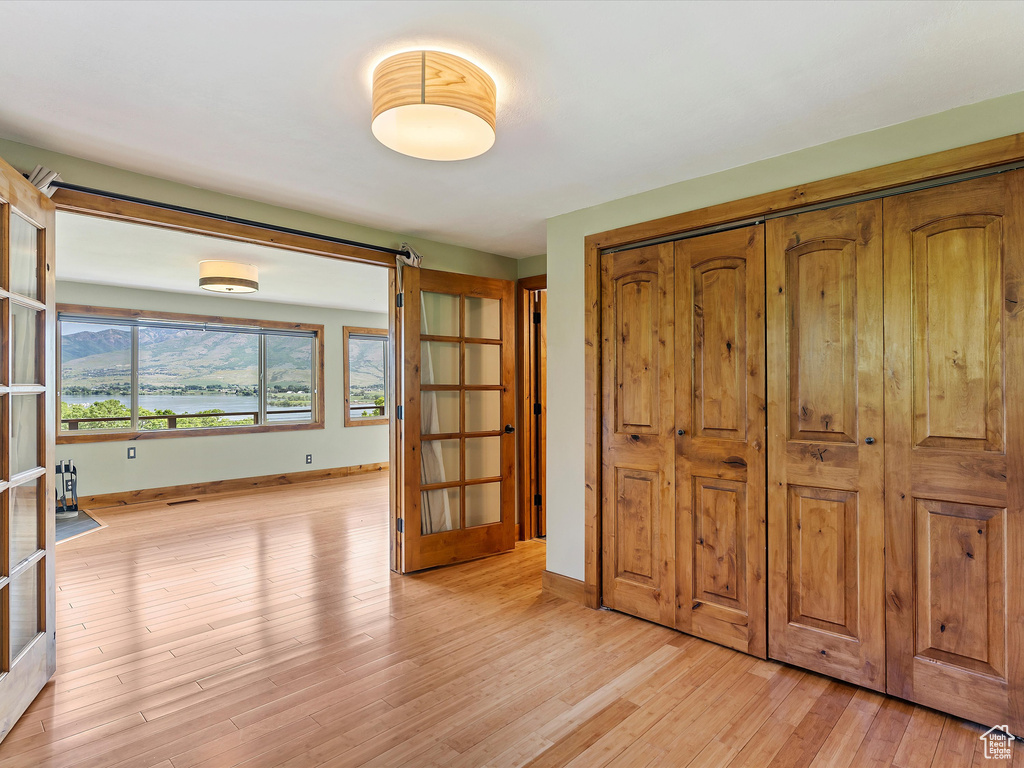 Unfurnished bedroom featuring baseboards, a closet, light wood-style floors, and french doors