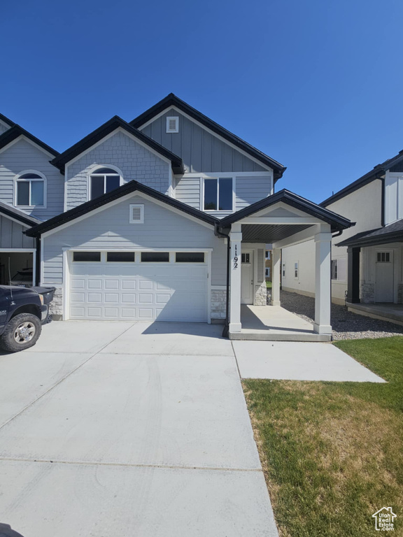View of front of home featuring driveway, covered porch, an attached garage, board and batten siding, and a front lawn