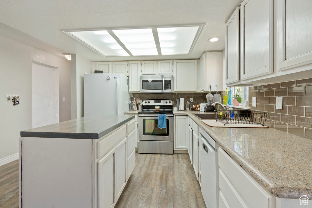 Kitchen featuring stainless steel appliances, light wood-style flooring, decorative backsplash, white cabinets, and recessed lighting