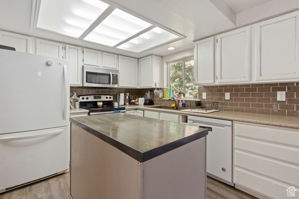 Kitchen with appliances with stainless steel finishes, a sink, decorative backsplash, white cabinetry, and light wood-style floors