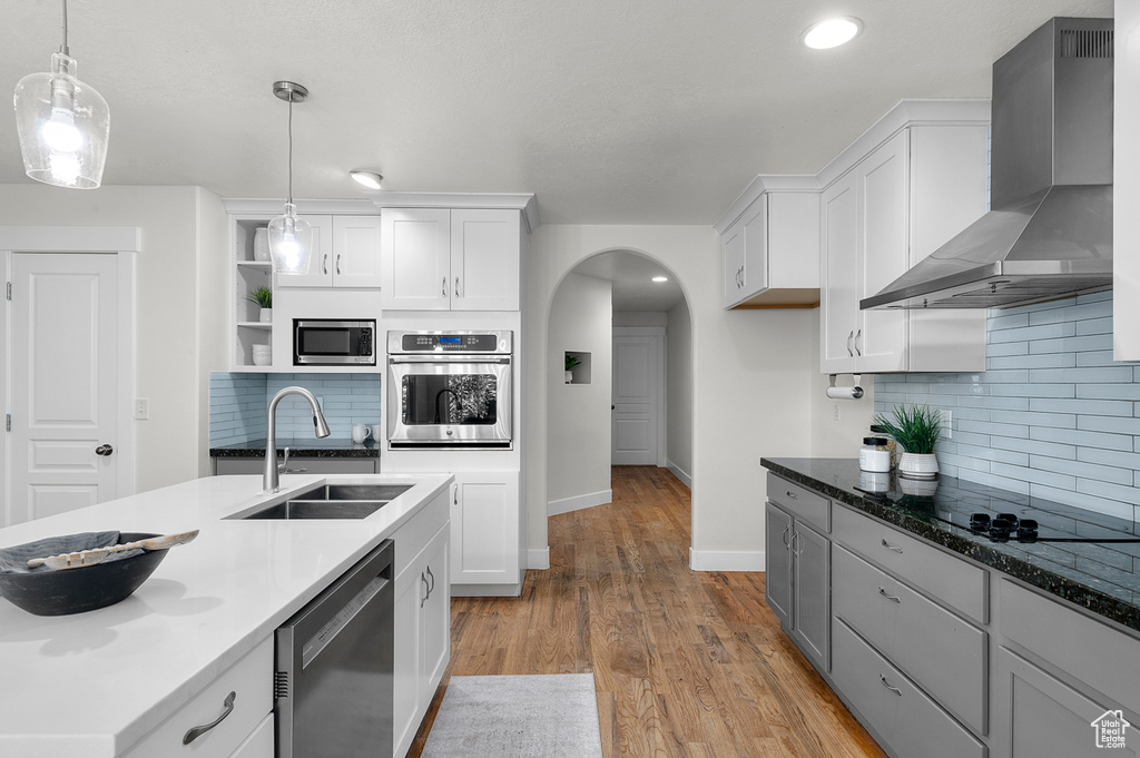 Kitchen with wall chimney range hood, stainless steel appliances, a sink, white cabinetry, and tasteful backsplash
