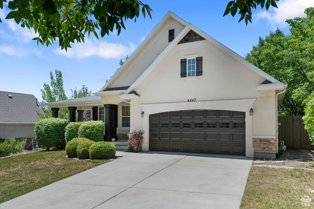 View of front facade with stone siding, driveway, an attached garage, and stucco siding