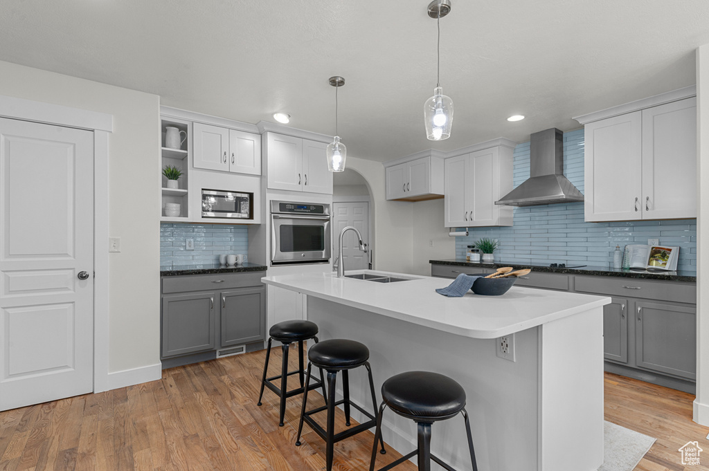 Kitchen featuring wall chimney exhaust hood, appliances with stainless steel finishes, a sink, open shelves, and tasteful backsplash