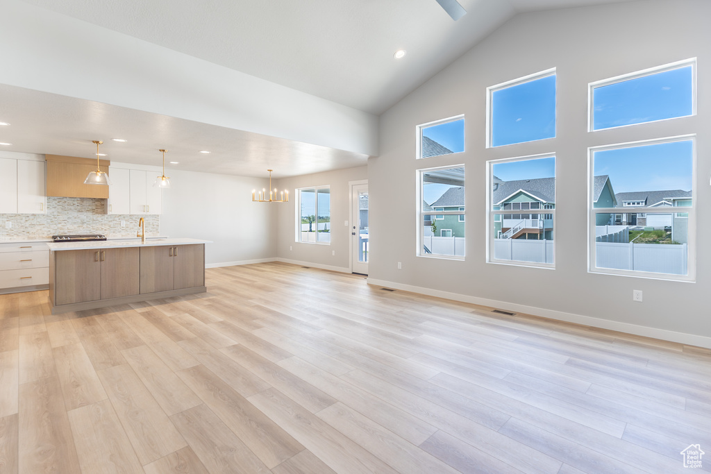 Unfurnished living room featuring a sink, a chandelier, light wood finished floors, baseboards, and recessed lighting