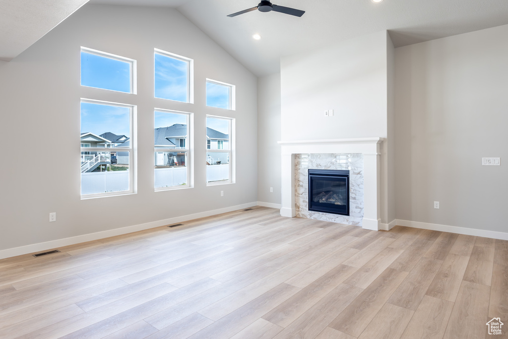 Unfurnished living room with a ceiling fan, plenty of natural light, high vaulted ceiling, a glass covered fireplace, and light wood-style flooring