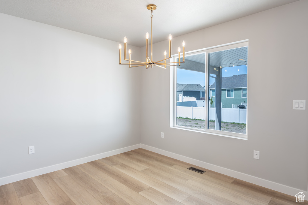Empty room featuring a chandelier, light wood-style flooring, and baseboards