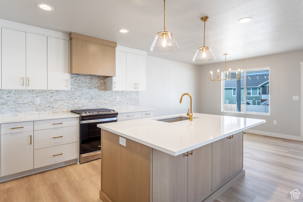Kitchen featuring stainless steel gas stove, a sink, light wood finished floors, decorative backsplash, and light countertops