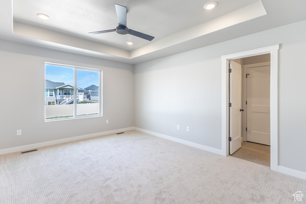 Unfurnished room with a tray ceiling, light carpet, ceiling fan, baseboards, and recessed lighting