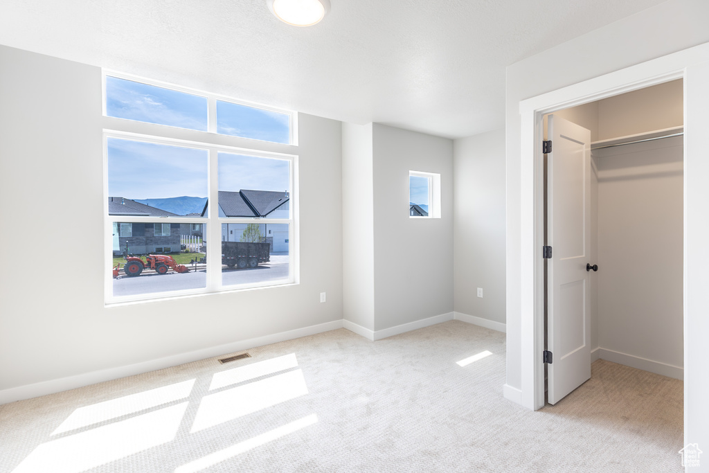 Unfurnished bedroom featuring light colored carpet, a walk in closet, and baseboards