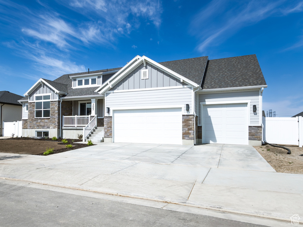 View of front of property featuring stone siding, a garage, board and batten siding, concrete driveway, and a residential view