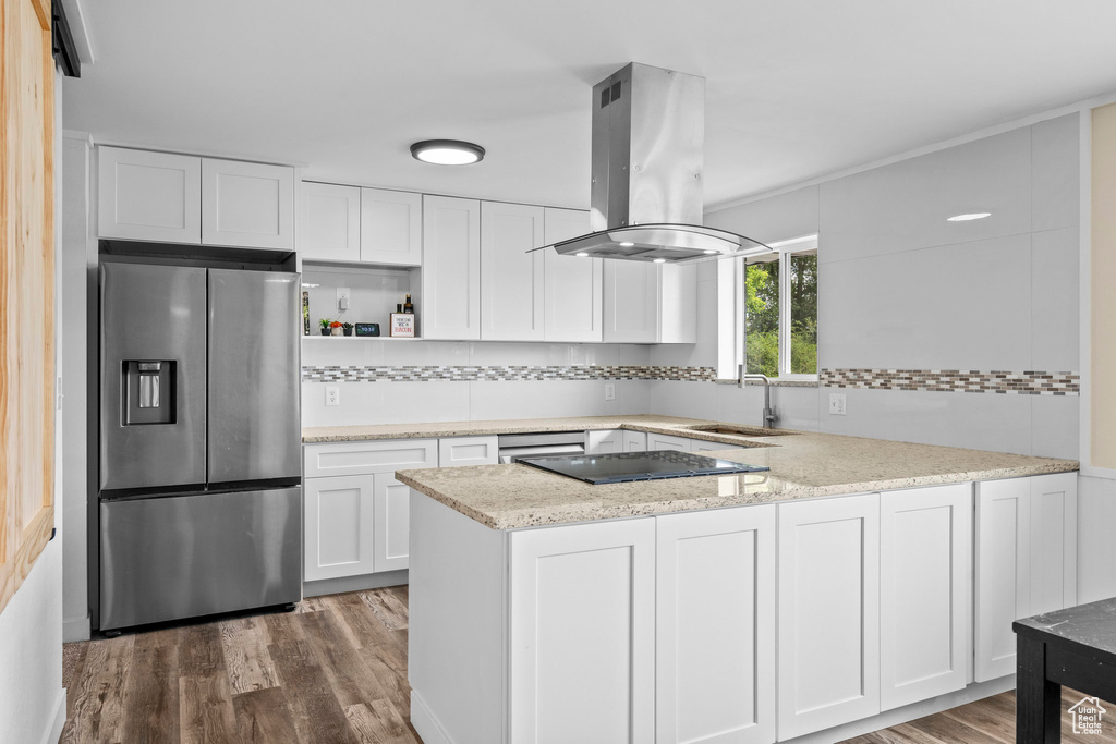 Kitchen featuring stainless steel fridge with ice dispenser, a sink, island range hood, a peninsula, and white cabinetry
