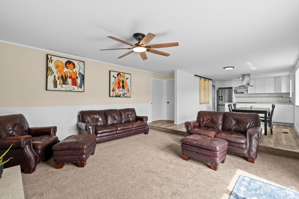 Living room with light colored carpet, a ceiling fan, a wainscoted wall, and ornamental molding