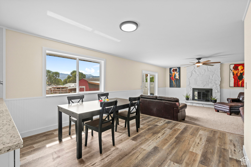 Dining room with a wainscoted wall, wood finished floors, a ceiling fan, and a fireplace