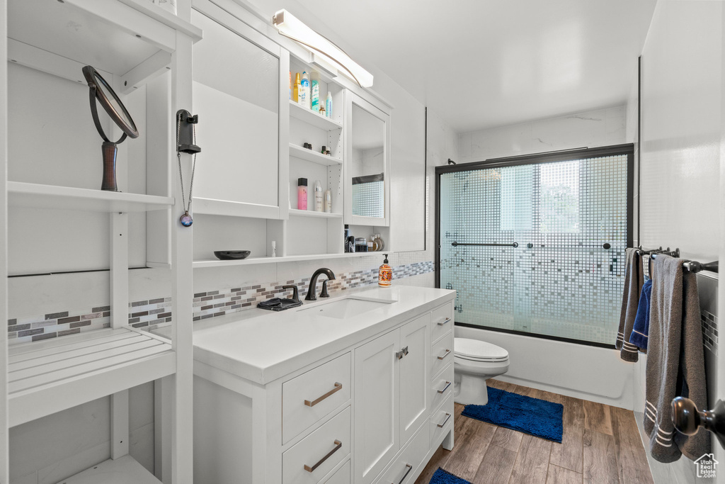Bathroom featuring toilet, enclosed tub / shower combo, vanity, backsplash, and wood finished floors