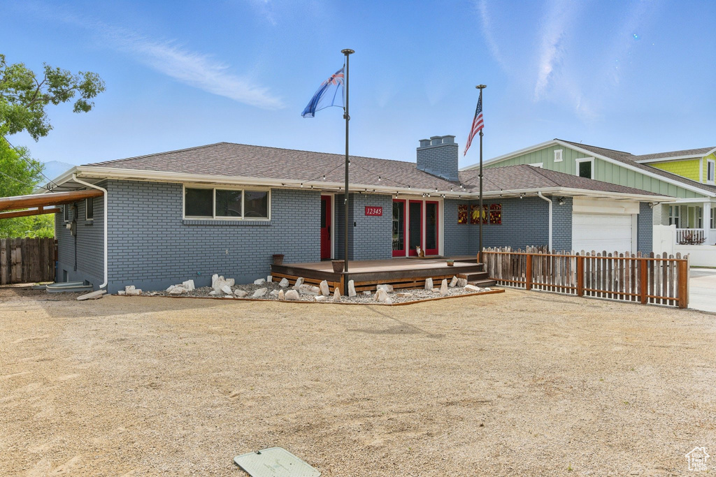 View of front of house with brick siding, a wooden deck, a garage, a chimney, and driveway