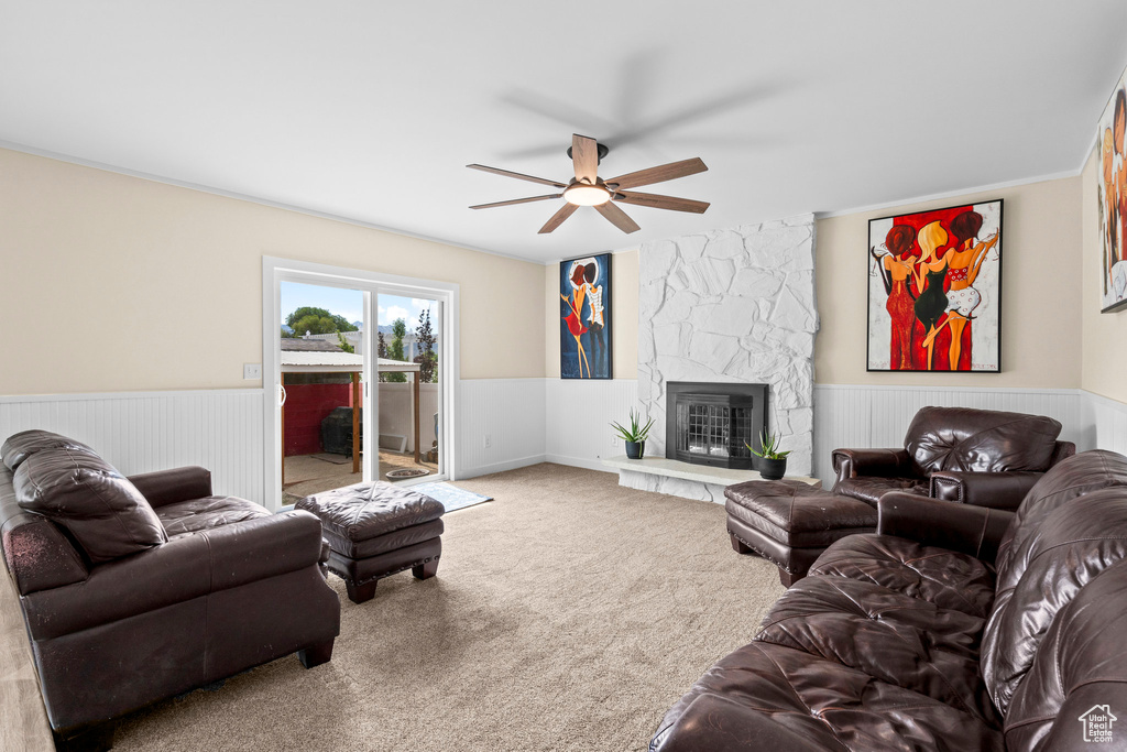 Carpeted living area featuring a wainscoted wall, a stone fireplace, a ceiling fan, and ornamental molding