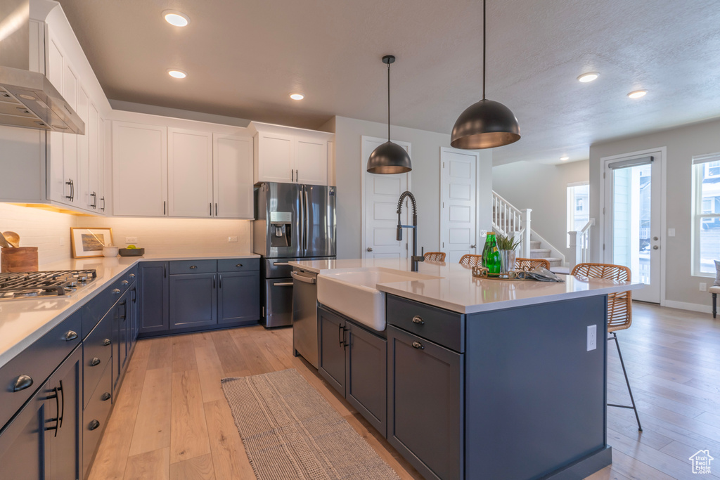 Kitchen with a sink, wall chimney exhaust hood, stainless steel appliances, a kitchen breakfast bar, and light wood finished floors