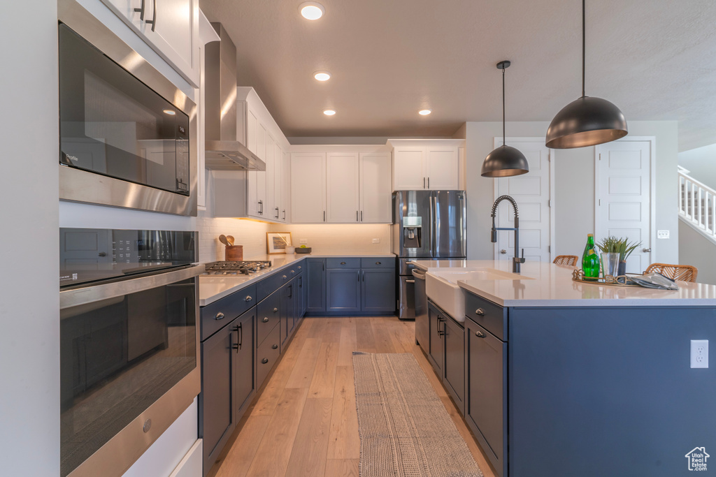 Kitchen featuring stainless steel appliances, a sink, wall chimney exhaust hood, light countertops, and white cabinets