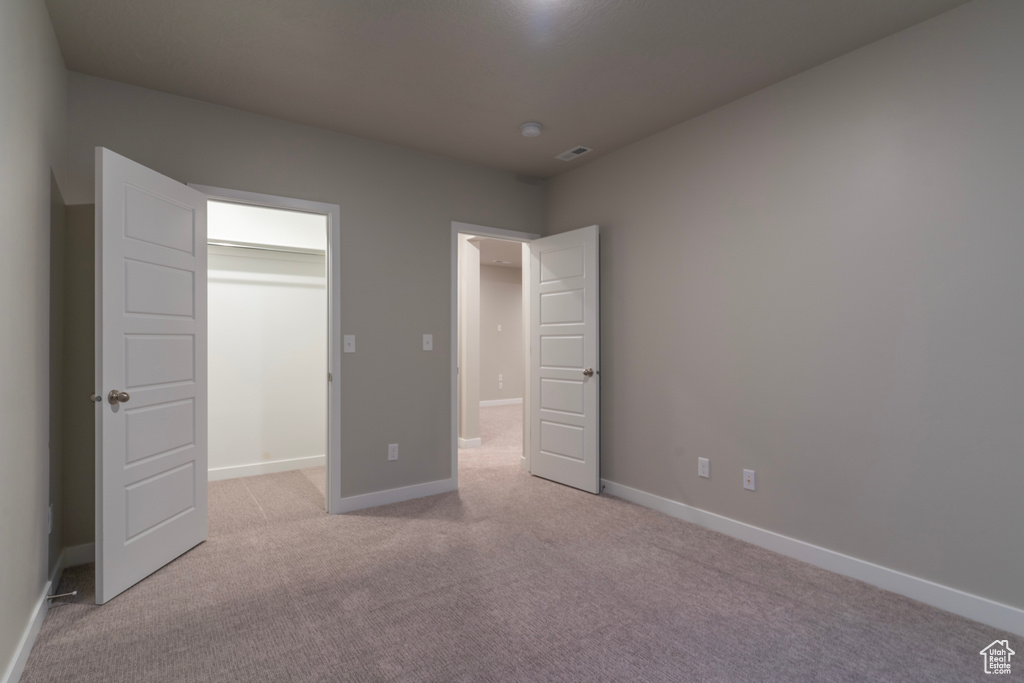 Unfurnished bedroom with light colored carpet, a spacious closet, and baseboards