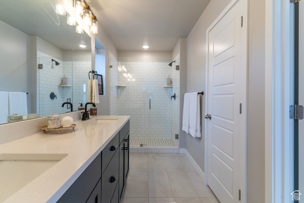 Bathroom featuring tile patterned floors, double vanity, a stall shower, and baseboards