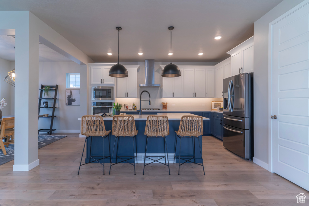 Kitchen featuring stainless steel appliances, wall chimney range hood, light countertops, white cabinetry, and recessed lighting