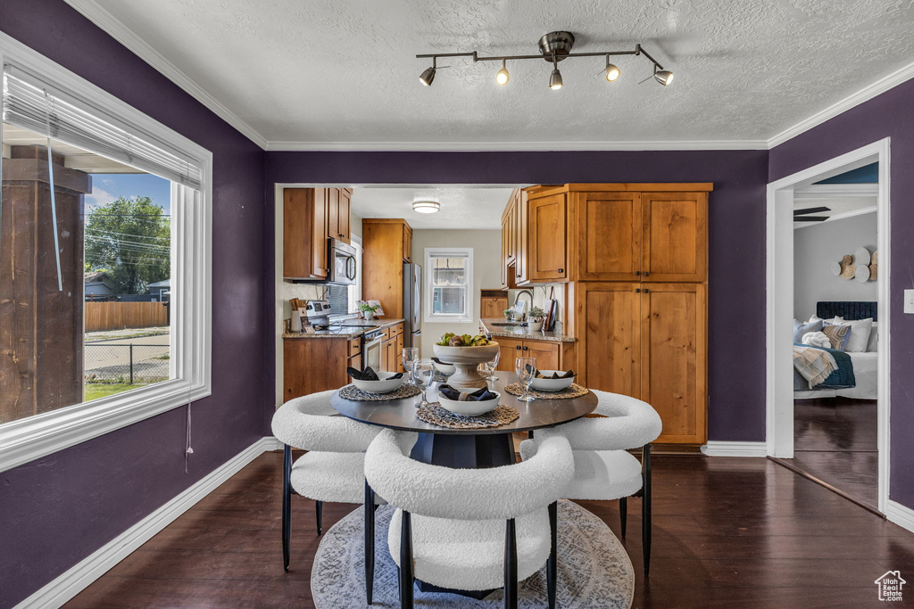 Dining area featuring dark wood-style flooring, baseboards, a textured ceiling, and ornamental molding