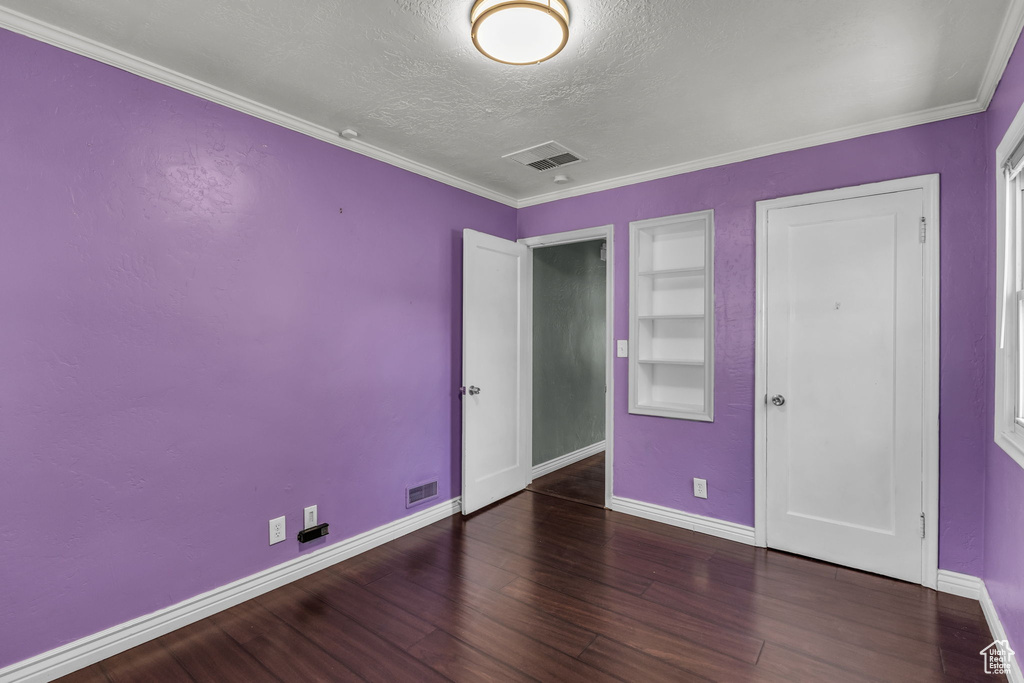 Unfurnished bedroom featuring a textured ceiling, baseboards, wood finished floors, and ornamental molding