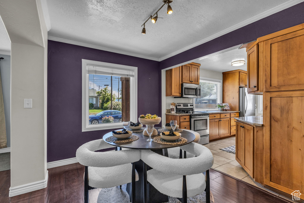 Dining room with light wood-style flooring, a textured ceiling, baseboards, track lighting, and ornamental molding