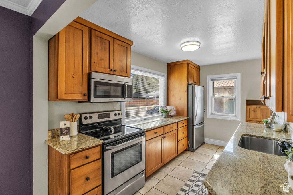 Kitchen featuring appliances with stainless steel finishes, plenty of natural light, a sink, brown cabinets, and a textured ceiling
