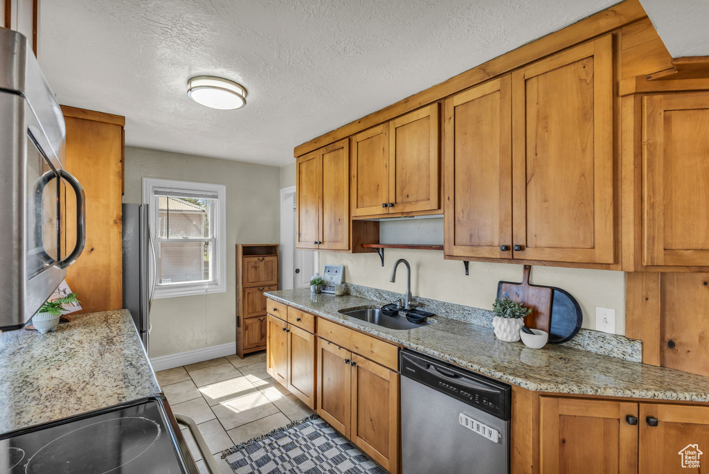 Kitchen featuring appliances with stainless steel finishes, a sink, brown cabinets, light tile patterned floors, and a textured ceiling