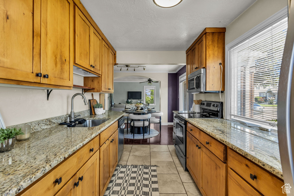 Kitchen featuring appliances with stainless steel finishes, a sink, ceiling fan, brown cabinets, and light stone counters