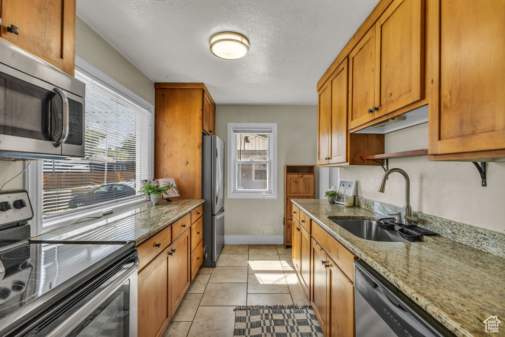 Kitchen with stainless steel appliances, a sink, brown cabinetry, baseboards, and light stone counters