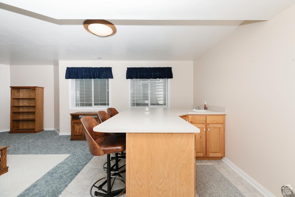 Kitchen featuring a breakfast bar, light countertops, a peninsula, baseboards, and a sink