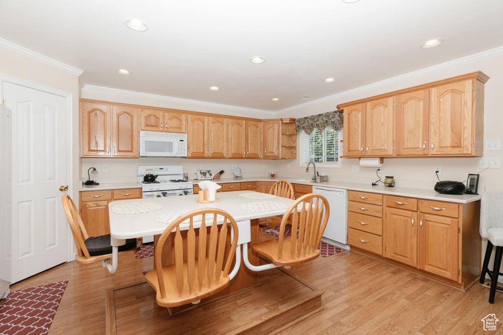 Kitchen with white appliances, a breakfast bar, a sink, ornamental molding, and light countertops