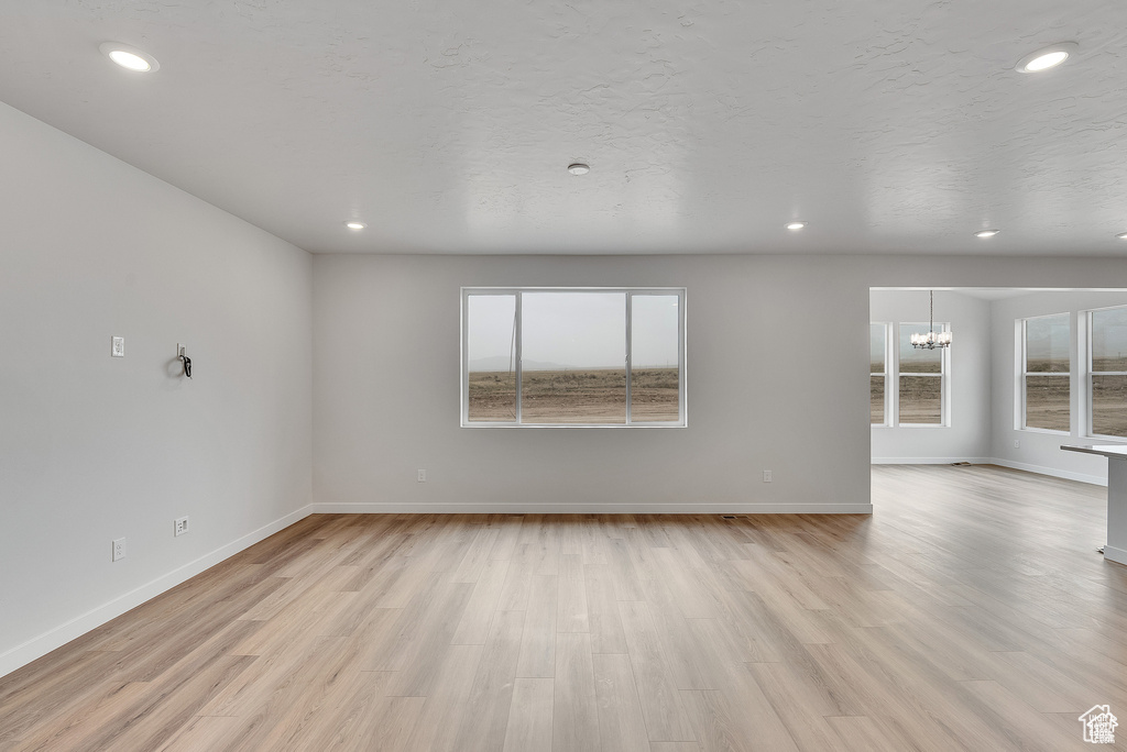 Unfurnished room with a chandelier, healthy amount of natural light, light wood finished floors, baseboards, and recessed lighting