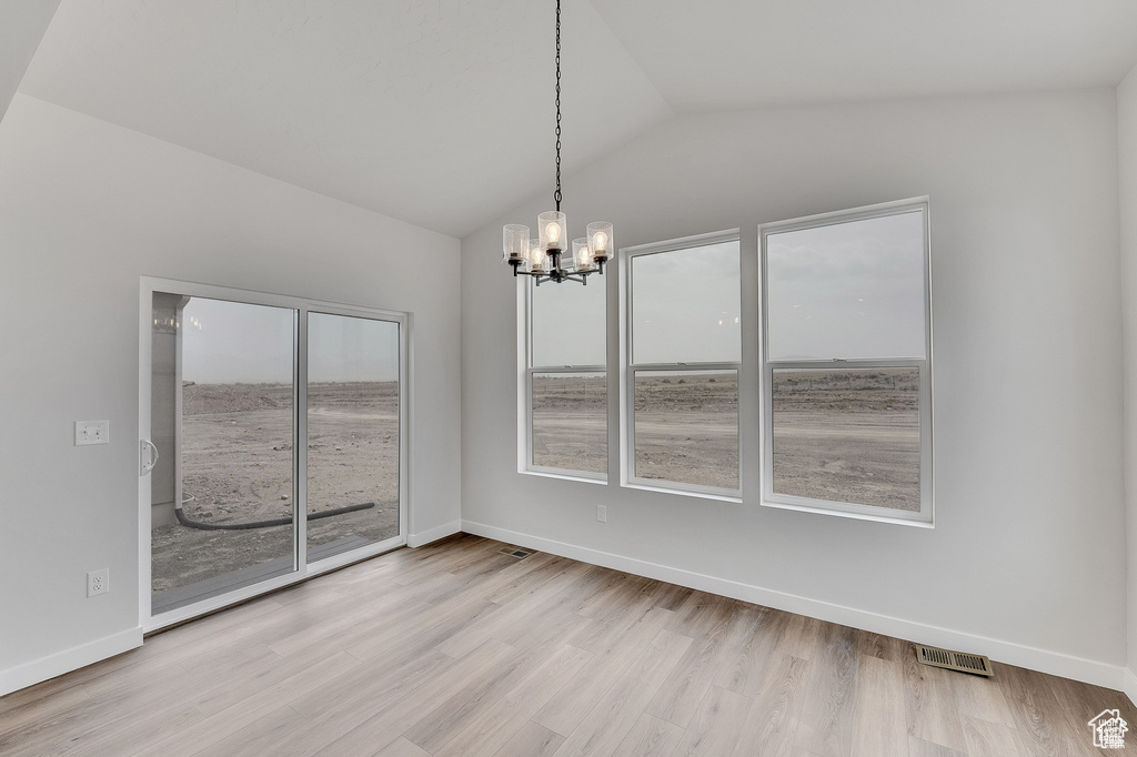 Unfurnished dining area featuring lofted ceiling, a chandelier, wood finished floors, and baseboards