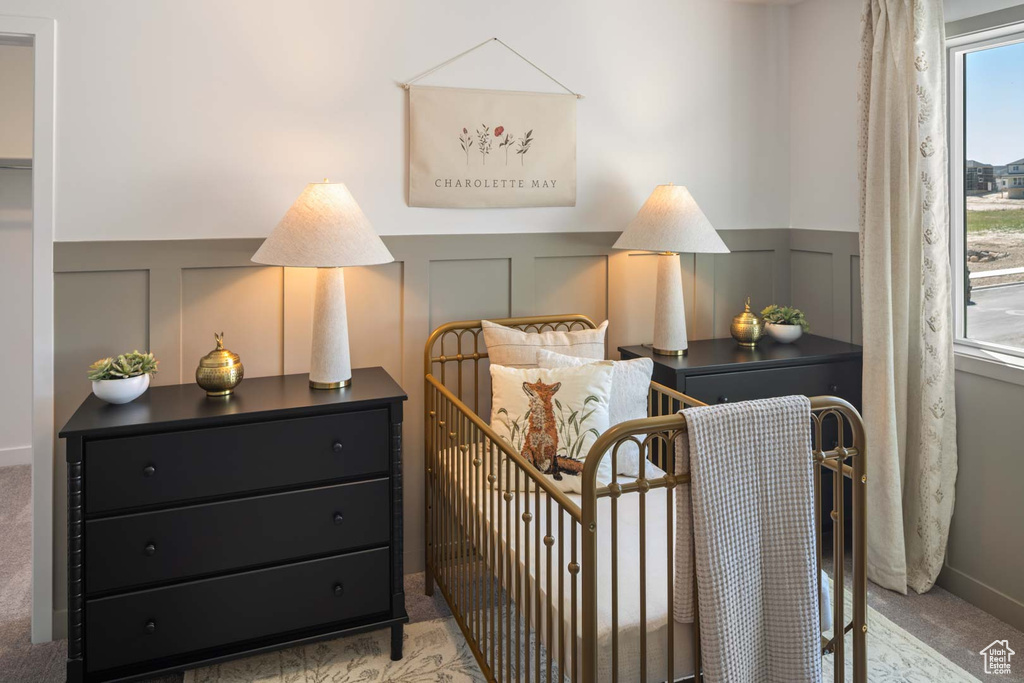 Bedroom featuring light colored carpet, a decorative wall, and a wainscoted wall