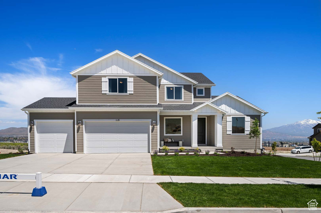 View of front facade with board and batten siding, a front lawn, driveway, a mountain view, and an attached garage