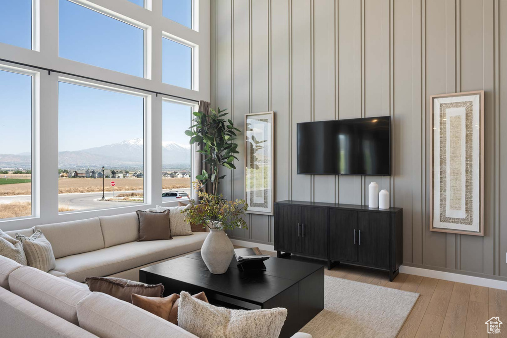 Living room featuring plenty of natural light, light wood-style floors, baseboards, a decorative wall, and a high ceiling