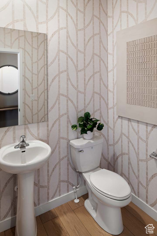 Bathroom featuring wallpapered walls, baseboards, wood finished floors, toilet, and a sink