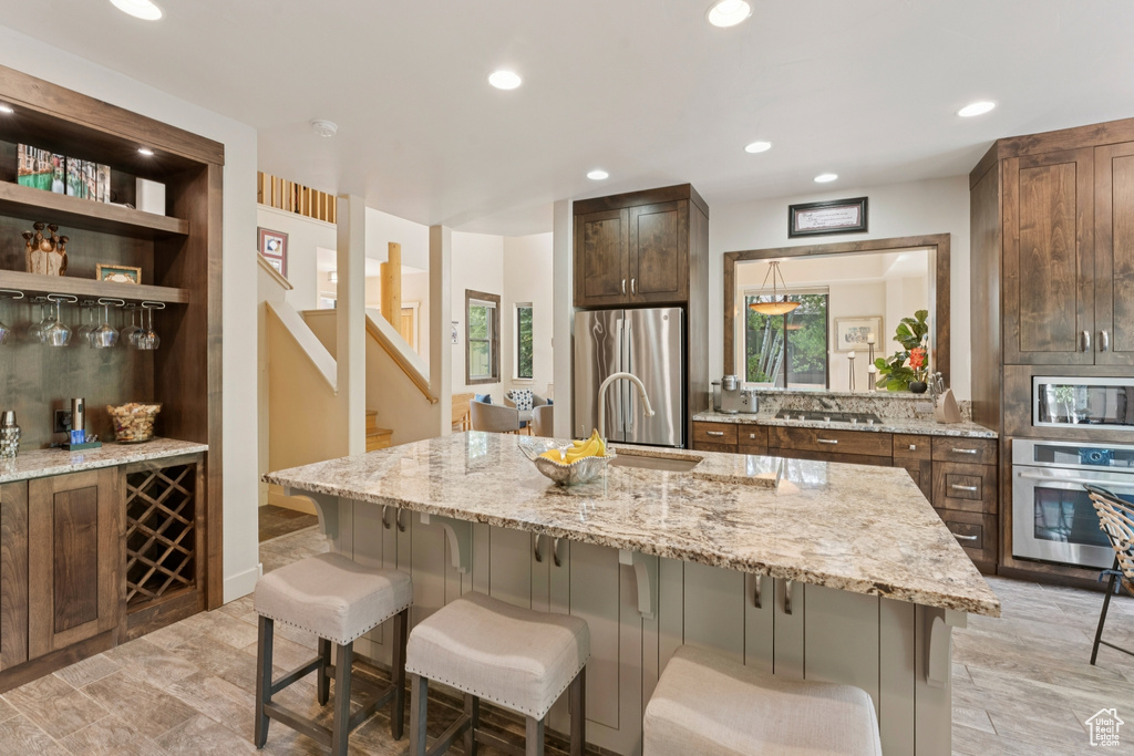 Kitchen with appliances with stainless steel finishes, a sink, a kitchen bar, light stone counters, and recessed lighting